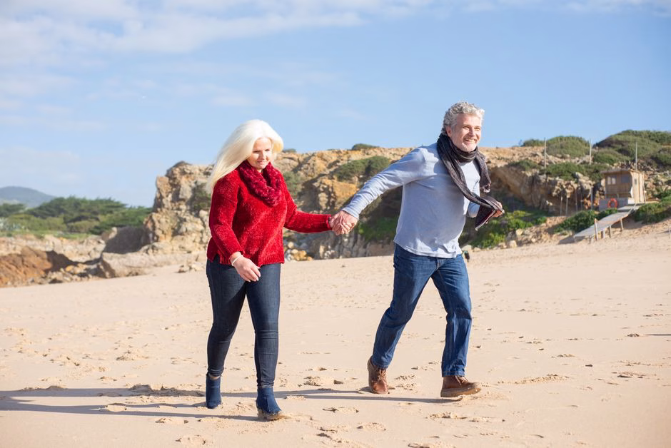 elderly couple walking beach sunset dunes Saúde e Bem-estar